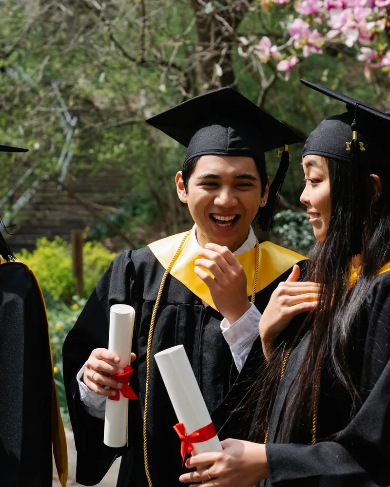 Graduates in caps and gowns laughing, holding their diplomas